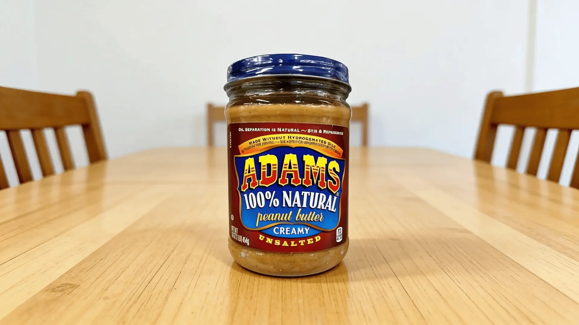 Adams 100 percent natural creamy peanut butter jar placed on wooden dining table with chairs in the background