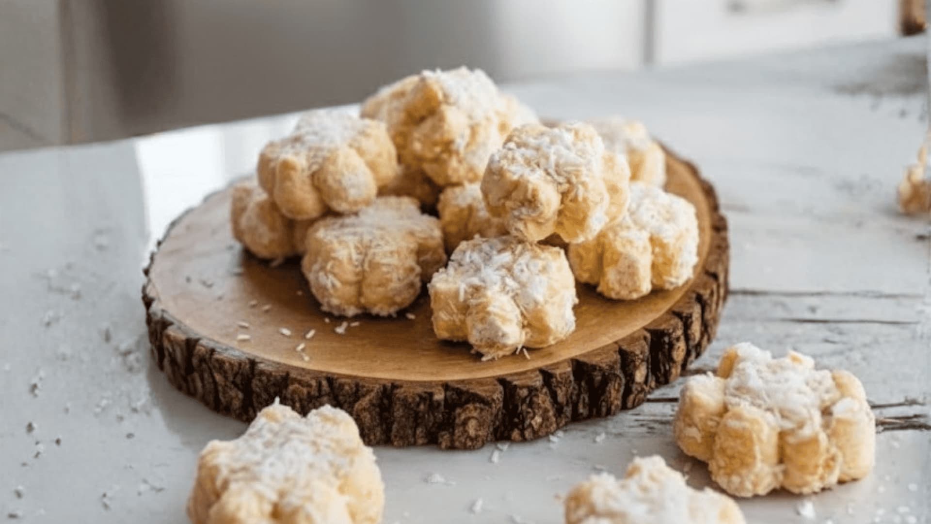 Flower-shaped coconut cookies on a wooden serving board in a bright, modern kitchen