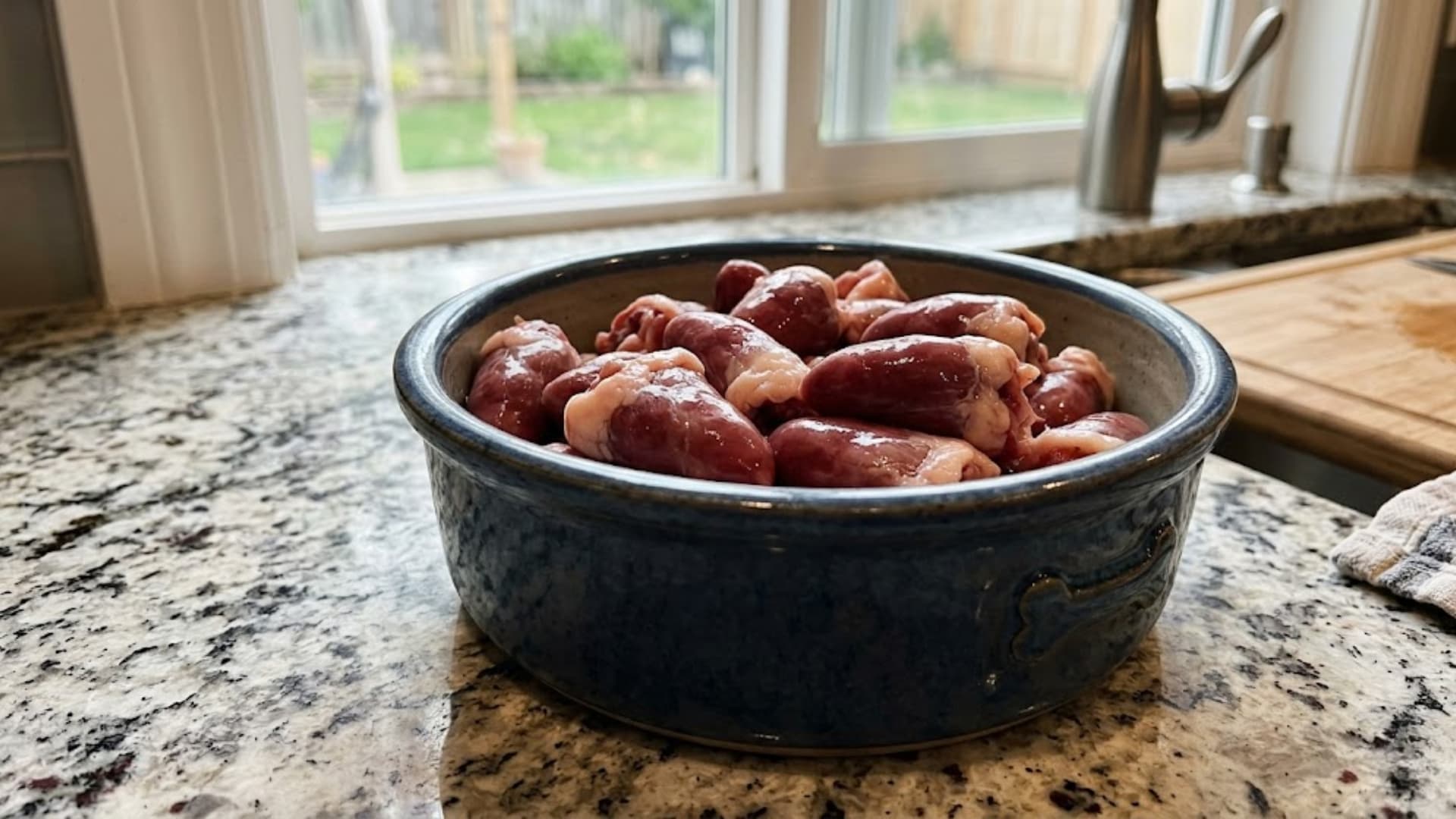 Fresh raw chicken hearts placed in a dog food bowl on a kitchen counter, clean setup, natural lighting
