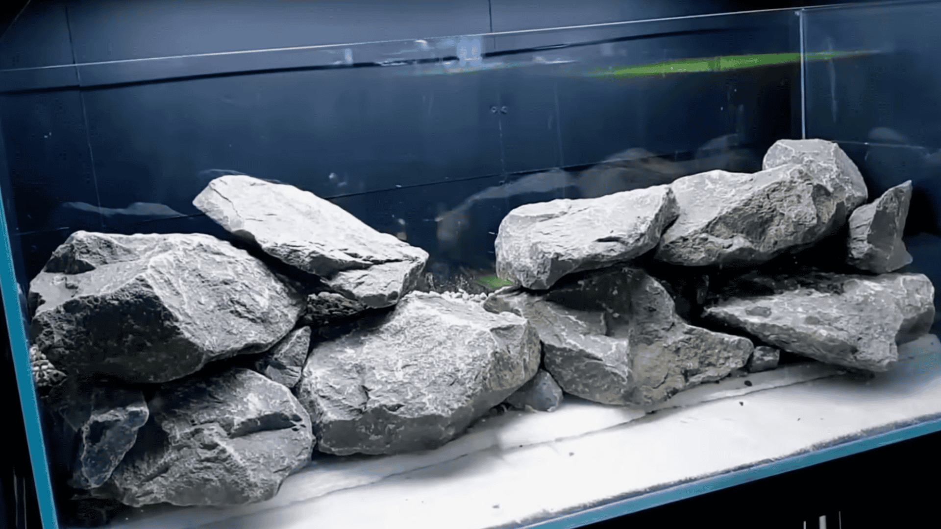 Glass aquarium with stacked gray rocks forming a hardscape, water partially filled, minimalistic aquascape setup