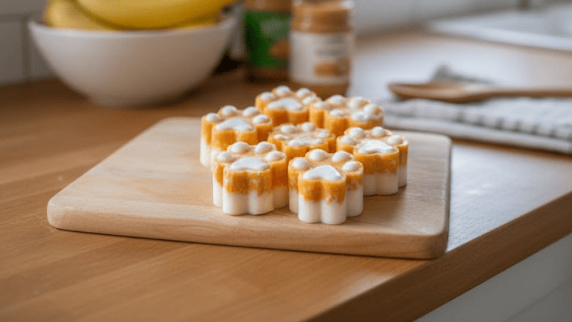 Paw-shaped peanut butter and banana frozen treats on a wooden board in a kitchen