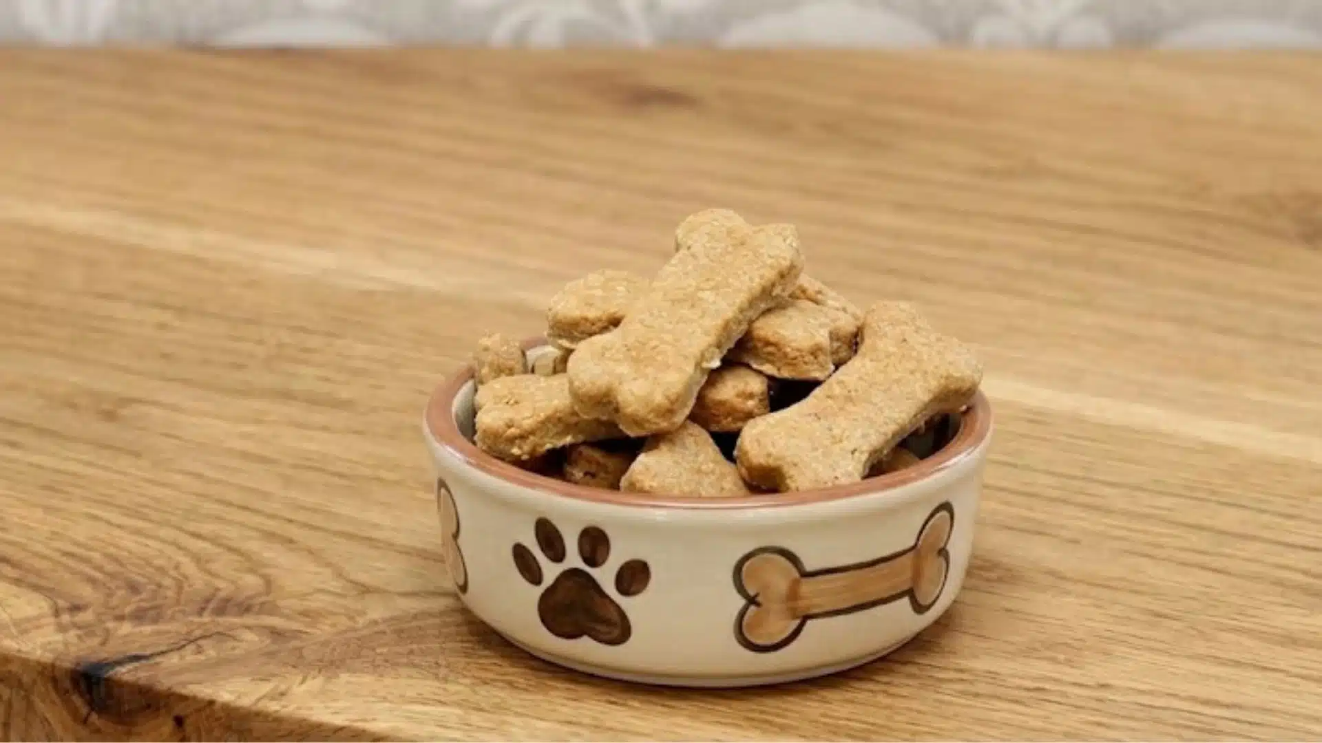 Peanut Butter and Banana Biscuits treats piled in a ceramic bowl with paw print and bone designs