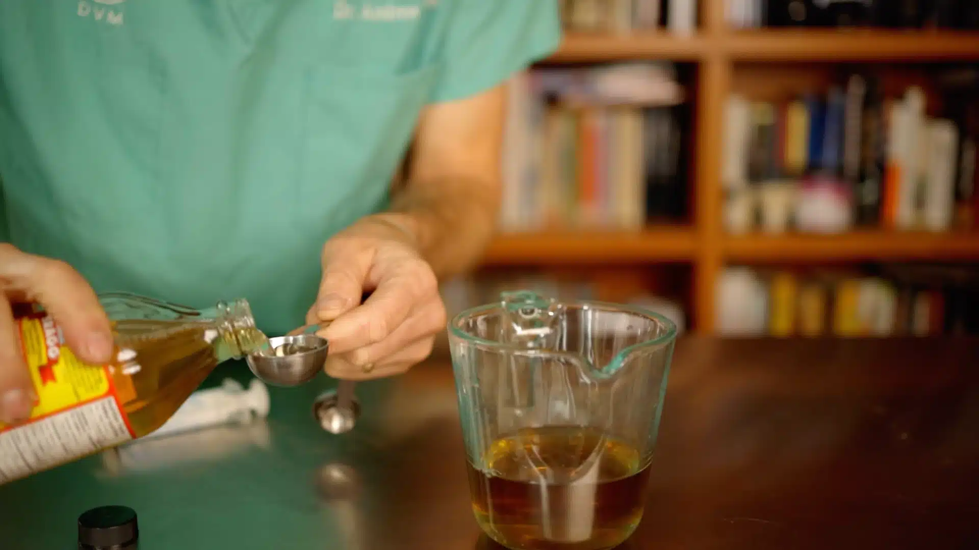 Person measuring apple cider vinegar into spoon beside glass cup of nettle tea for homemade dog ear cleaning solution