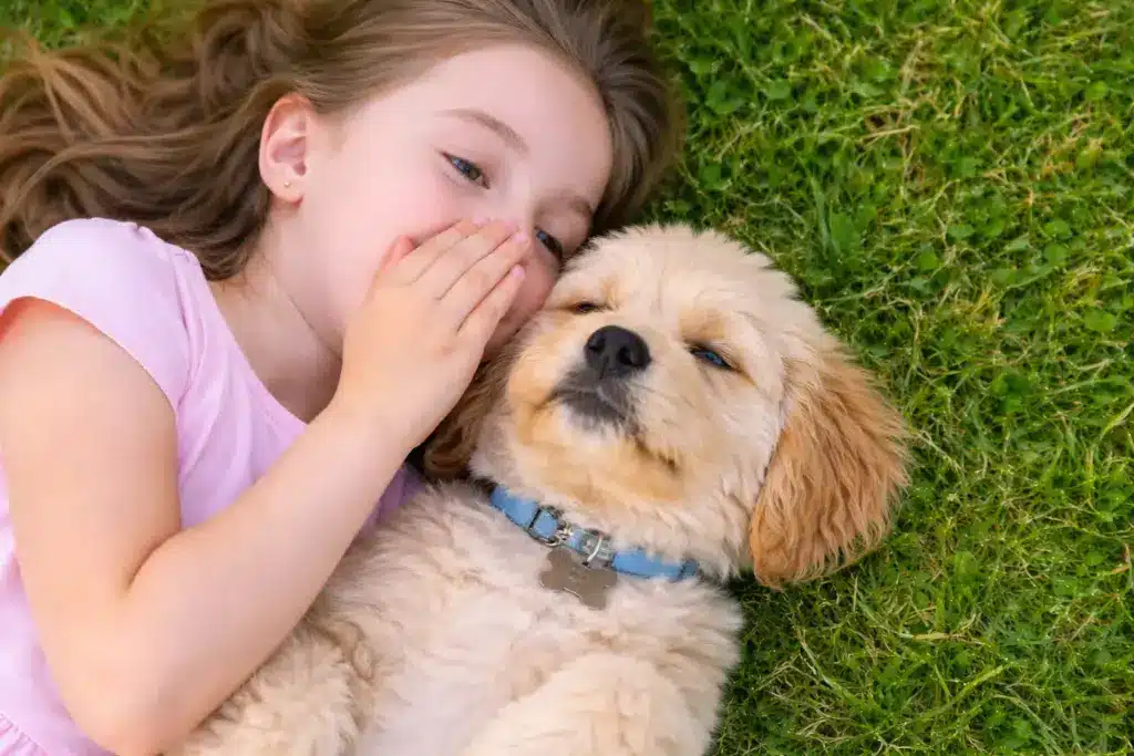 Young girl lying on grass whispering to her dog, suggesting communication and understanding between dogs and humans