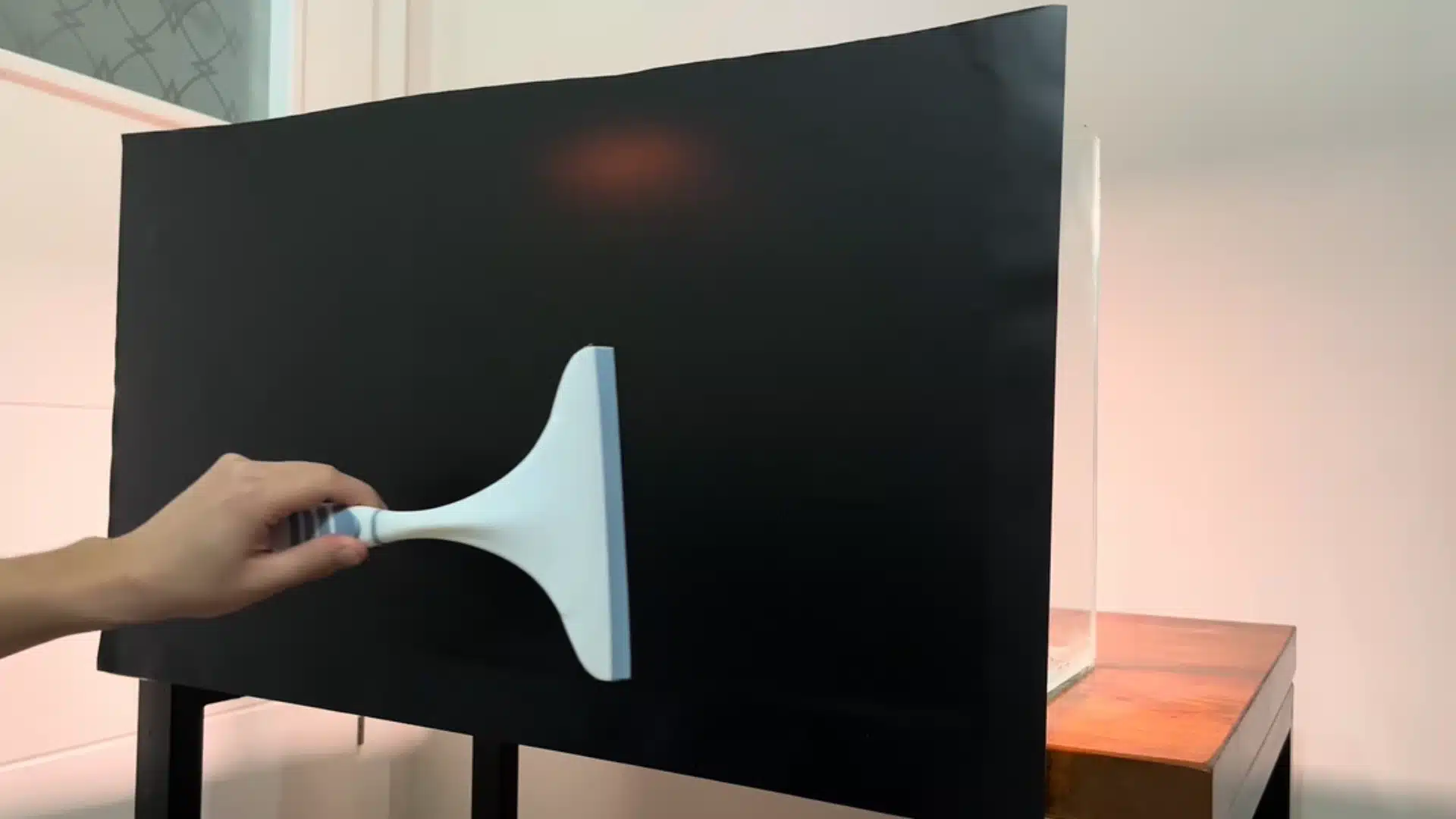 Hand uses a squeegee to apply a black background to an aquarium tank