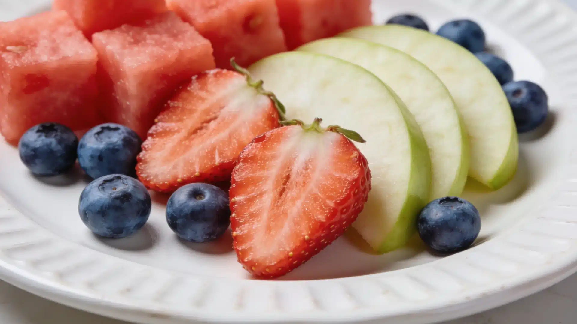 Plate of sliced fruit with watermelon, apple, berries, and strawberries