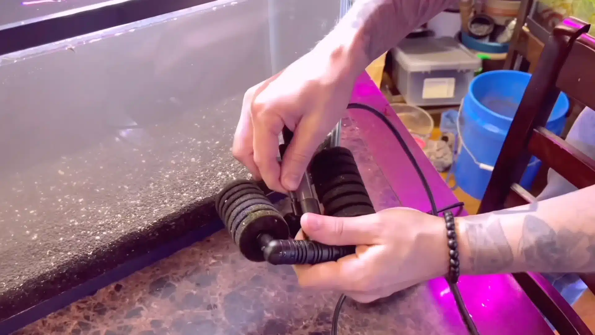 Tattooed hands assemble a double sponge filter next to a fish tank in